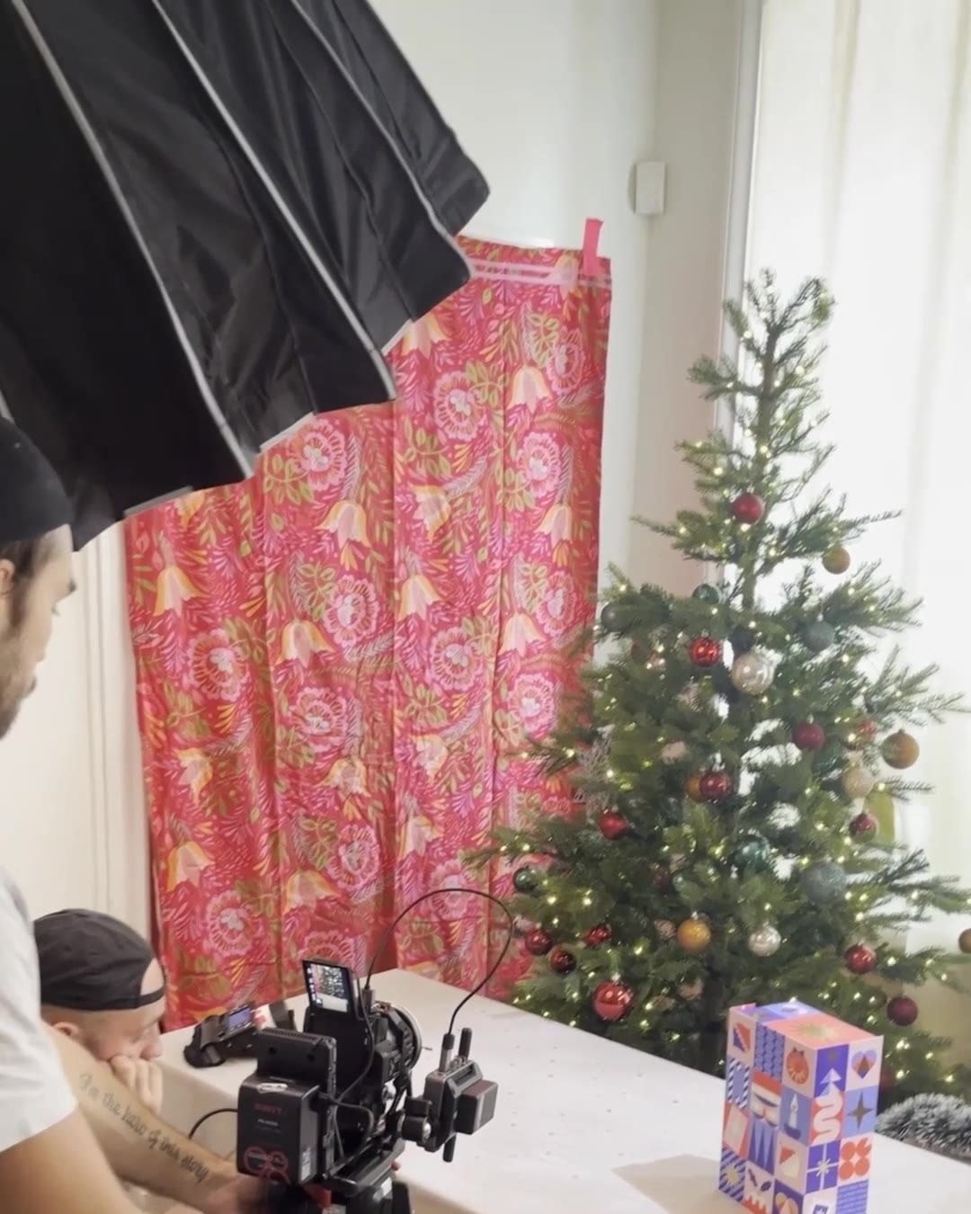 Filmteamet vid ett bord med en julkalender, en röd gardin och en julgran, med kameran på bordet och en stor softbox ovanför