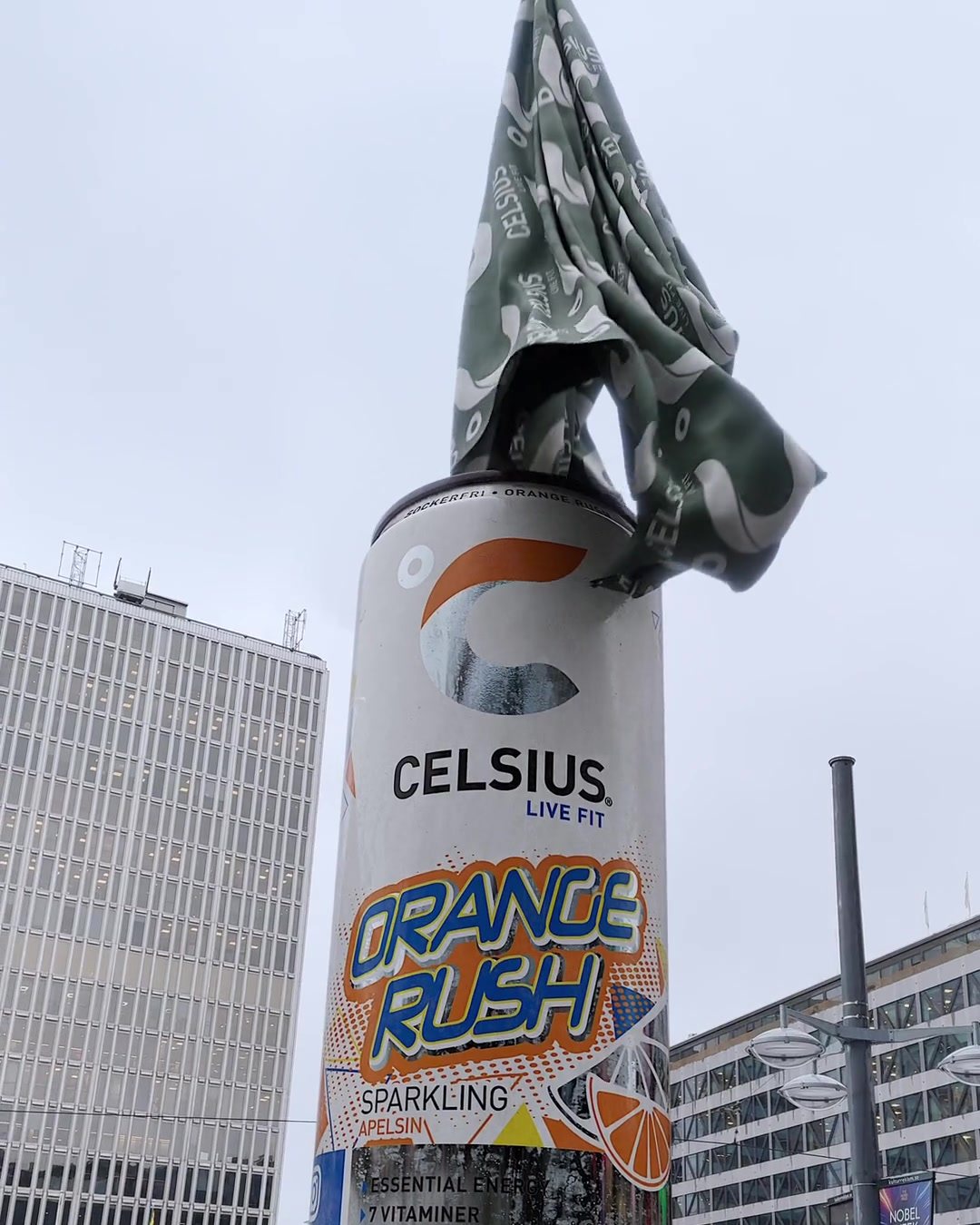A green Celsius cloth falls off a 20 metre Orange Rush can at Sergels torg while people watch